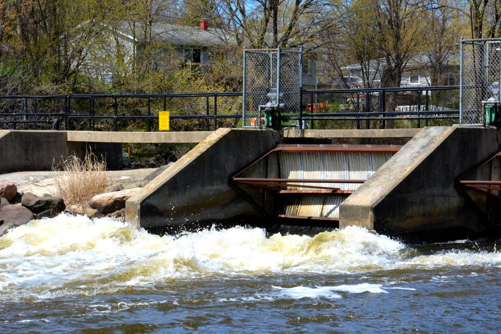 The dam at the Fox River in Rochester Wisconsin with the rapids just below the small dam rushing into the natural waterway on a clear spring day in April.